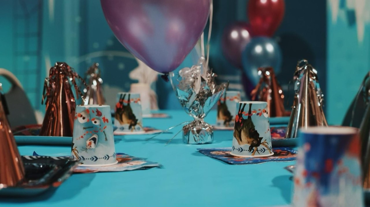 Frozen-themed birthday party table with Frozen-character cups, balloons, and Elsa backdrop
