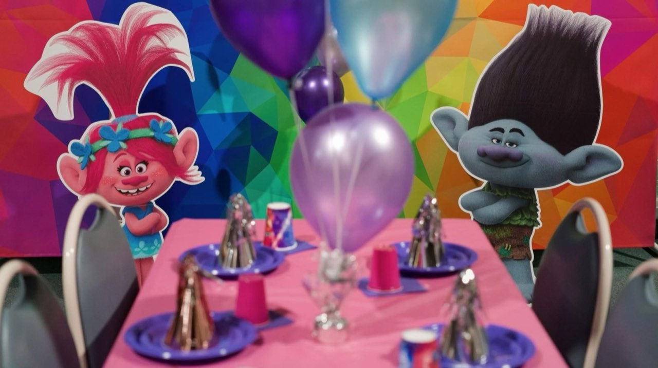 Trolls-themed party table with Poppy and Branch cardboard cutouts and rainbow backdrop