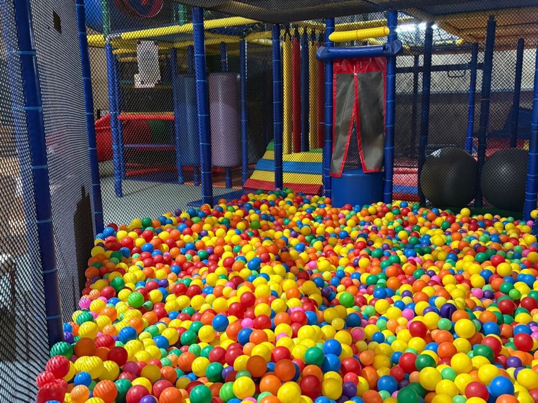 Large ball pit at Rumble Tumbles with multi-coloured plastic balls and climbing nets behind